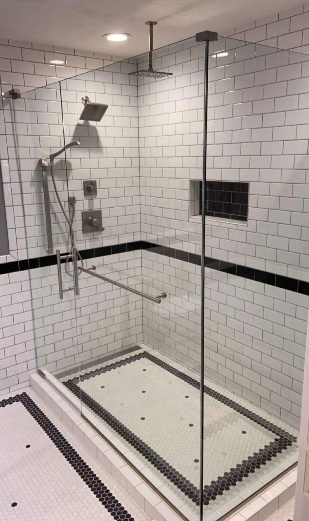 Glass shower with white subway tile, black trim, and a handheld showerhead in a tiled bathroom.