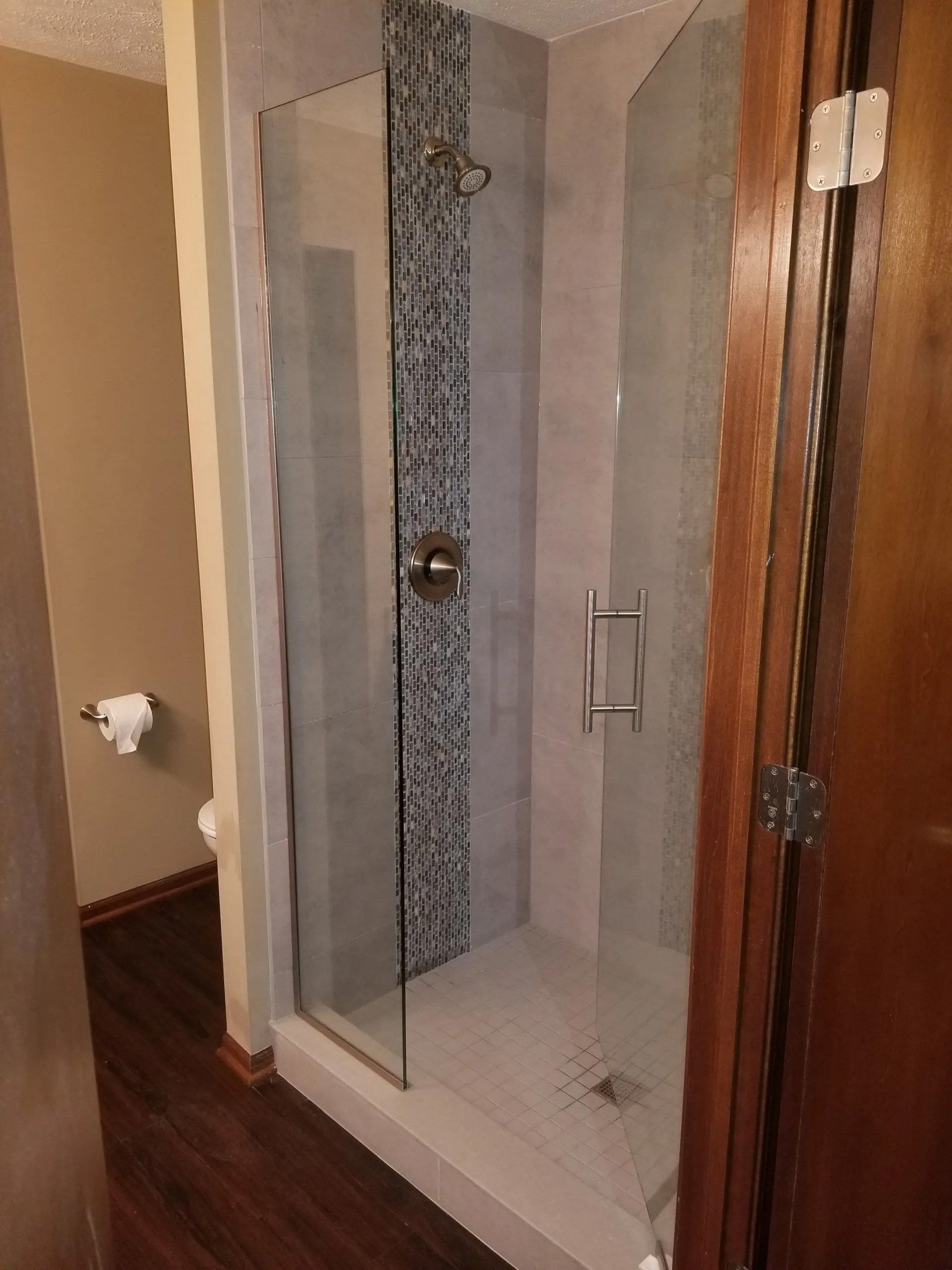 Bathroom with a glass shower enclosure and tiled floor next to a wooden door.