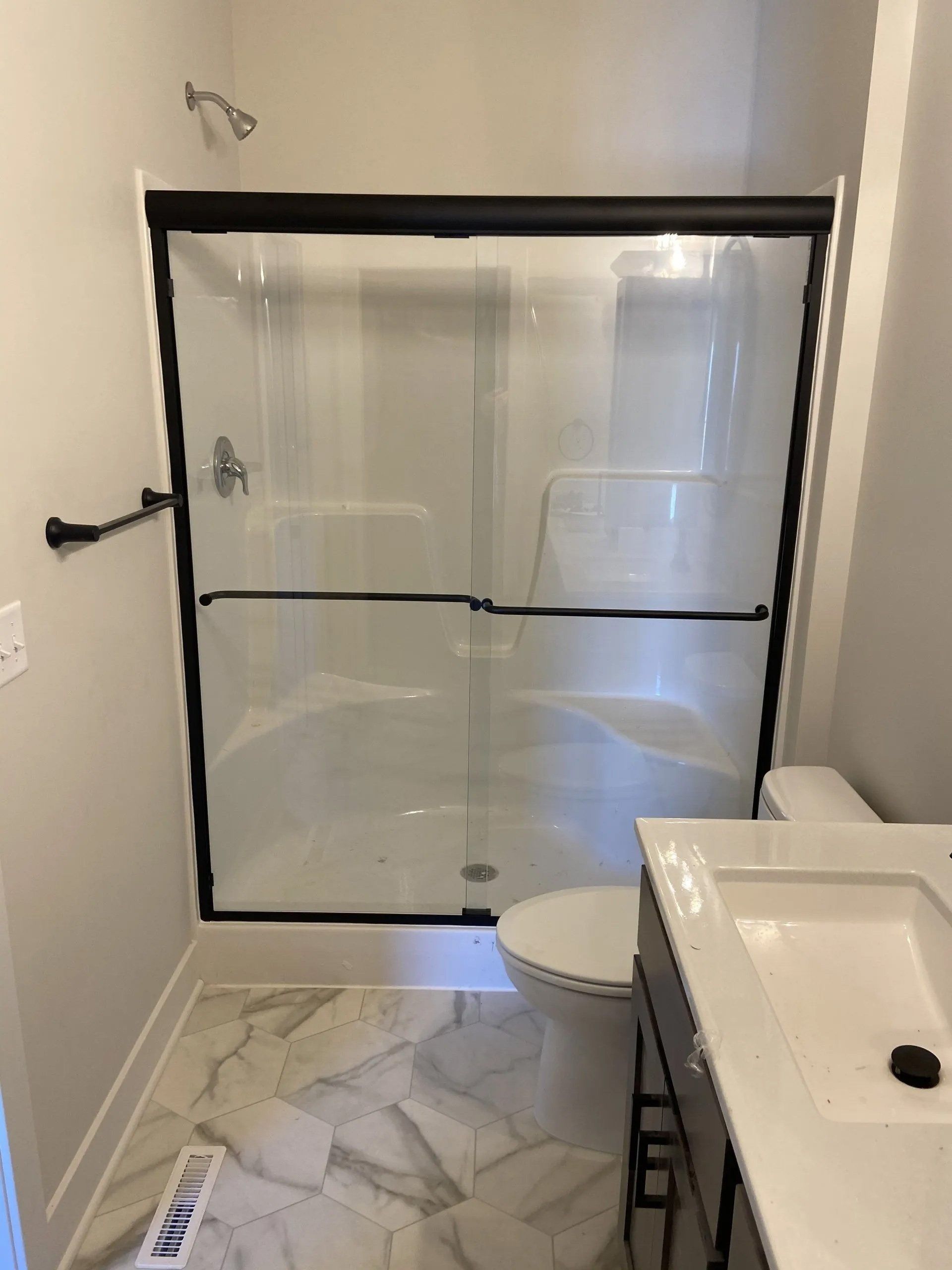Bathroom with glass shower enclosure, toilet, and white vanity on marble-pattern tile floor.