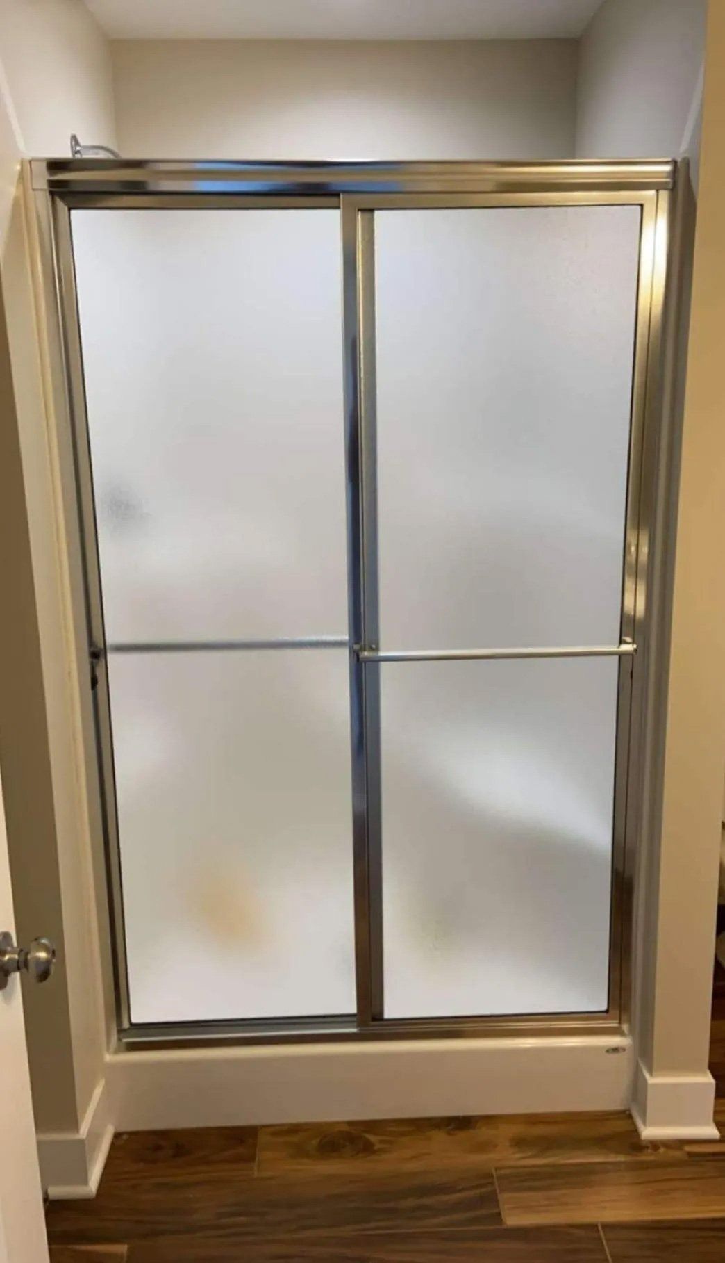 Brass-framed frosted glass shower door in a tiled bathroom doorway.