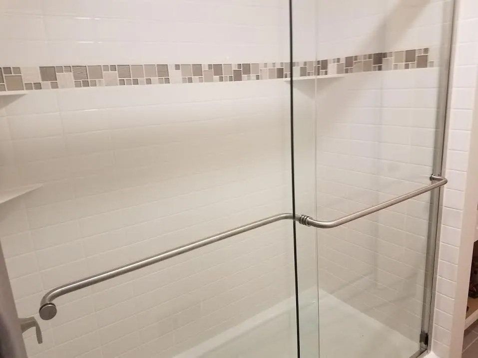 Glass shower enclosure with metal grab bars and white tiled walls