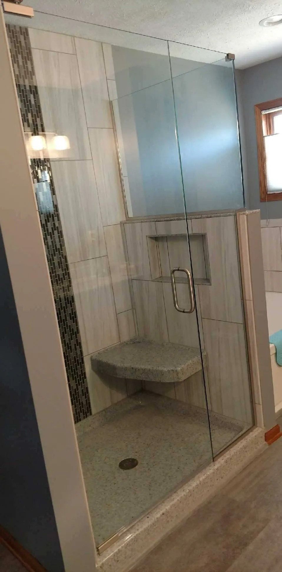 Small tiled shower stall with a glass door, built-in bench, and wall-mounted shower fixtures.