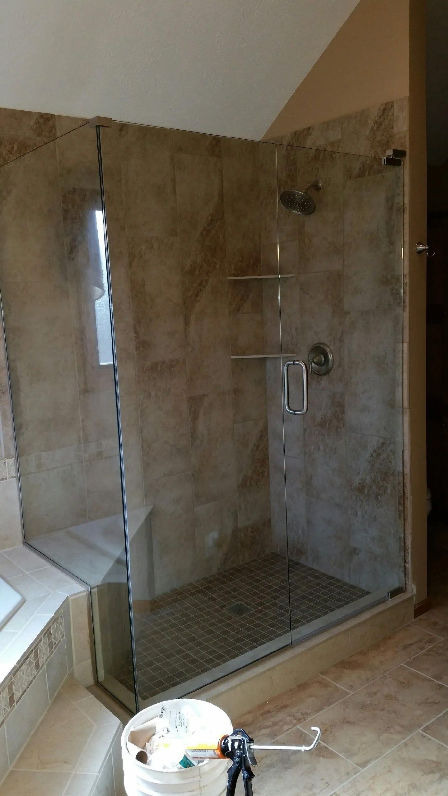 Tiled walk-in shower with glass partition, built-in shelves, and a handheld showerhead in a bathroom.