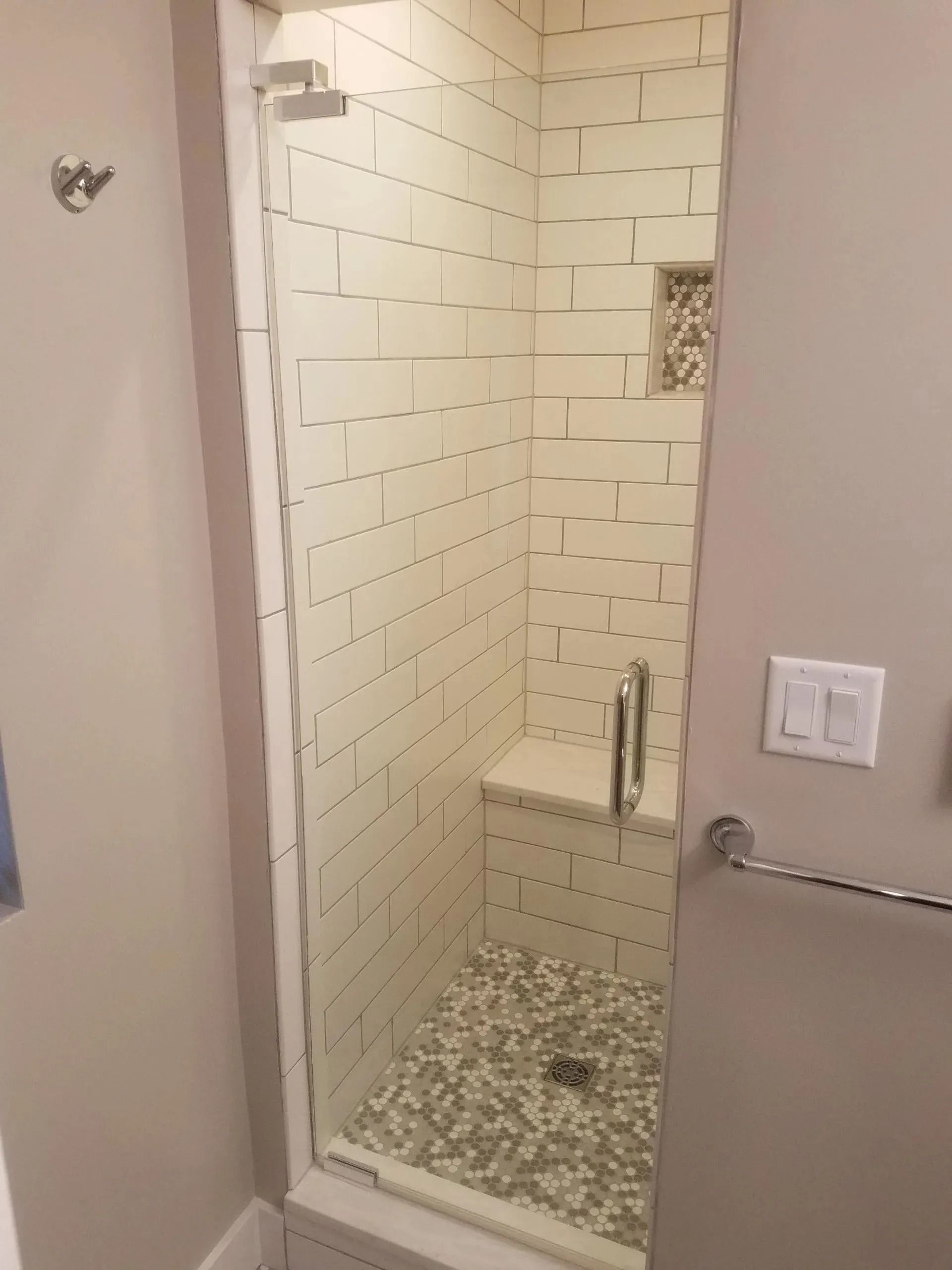 Tiled walk-in shower with pebble floor, built-in bench, and glass door frame in a bathroom