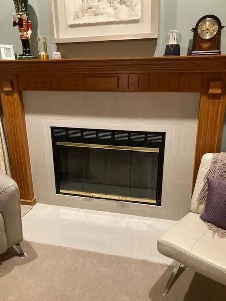 Living room fireplace with wooden mantel, white surround, and beige chairs nearby