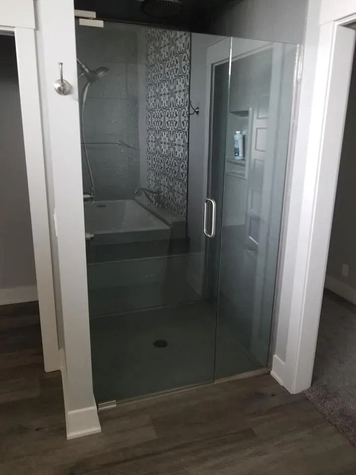Glass shower stall with sliding door in a bathroom, next to a patterned tile accent wall.
