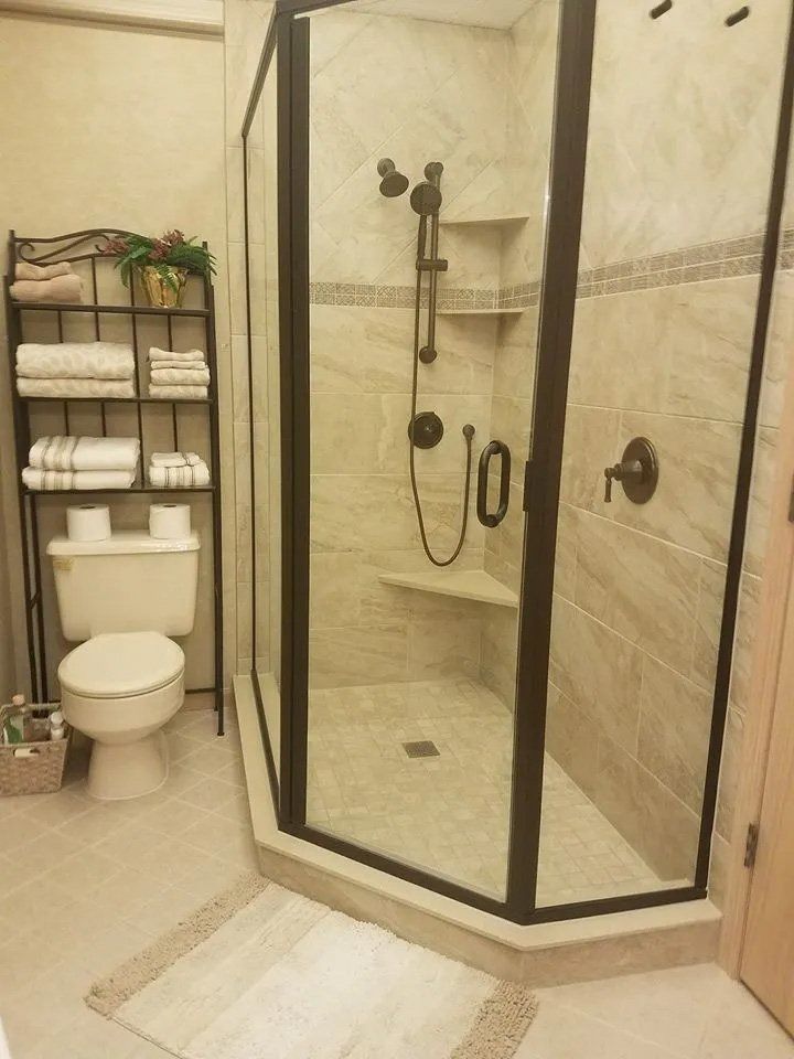 Bathroom with glass-enclosed shower, toilet, shelves of towels, and beige tile flooring.