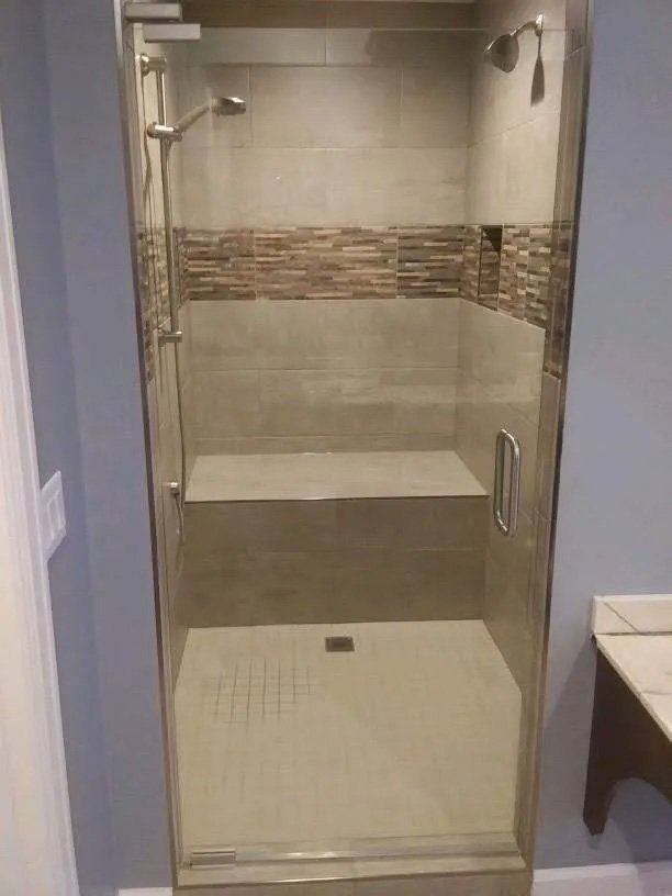 Glass walk-in shower with beige tile, built-in bench, and handheld showerhead