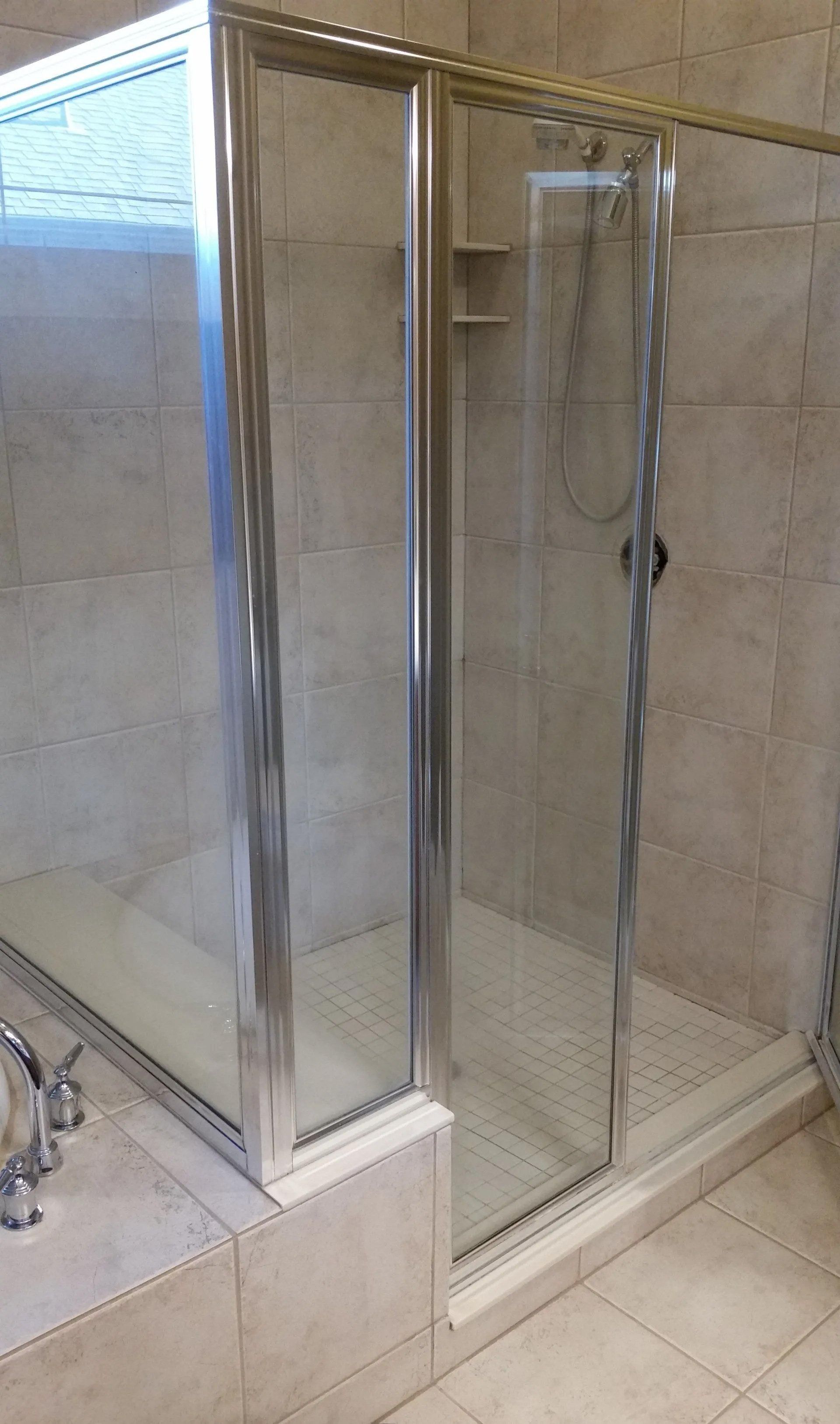 Glass-enclosed shower with tiled walls and a handheld showerhead in a beige bathroom