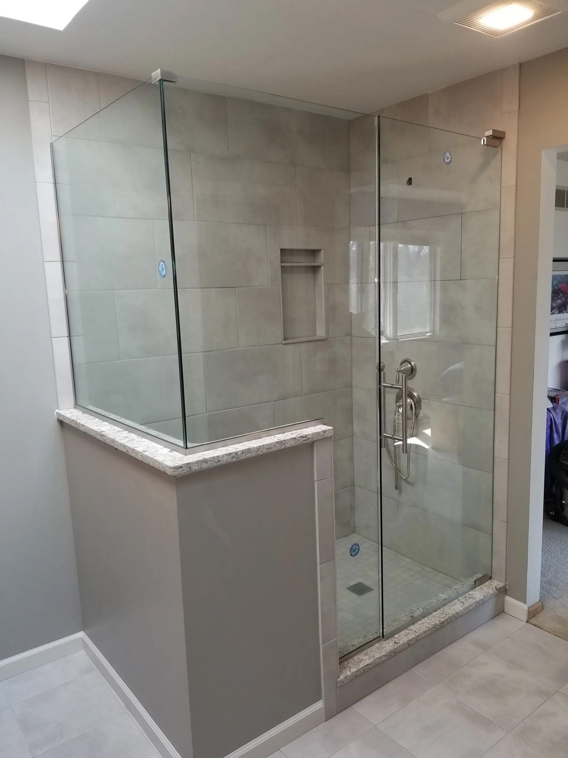 Glass shower enclosure in a gray-tiled bathroom with a marble ledge and chrome fixtures