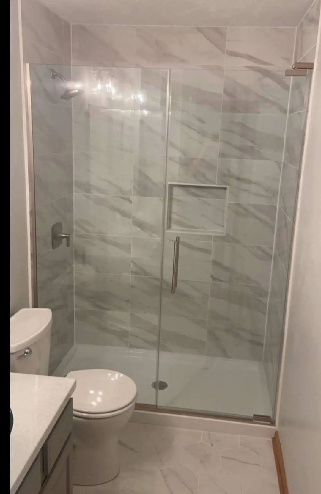Small bathroom with a glass shower enclosure and marble-look tile walls next to a toilet.