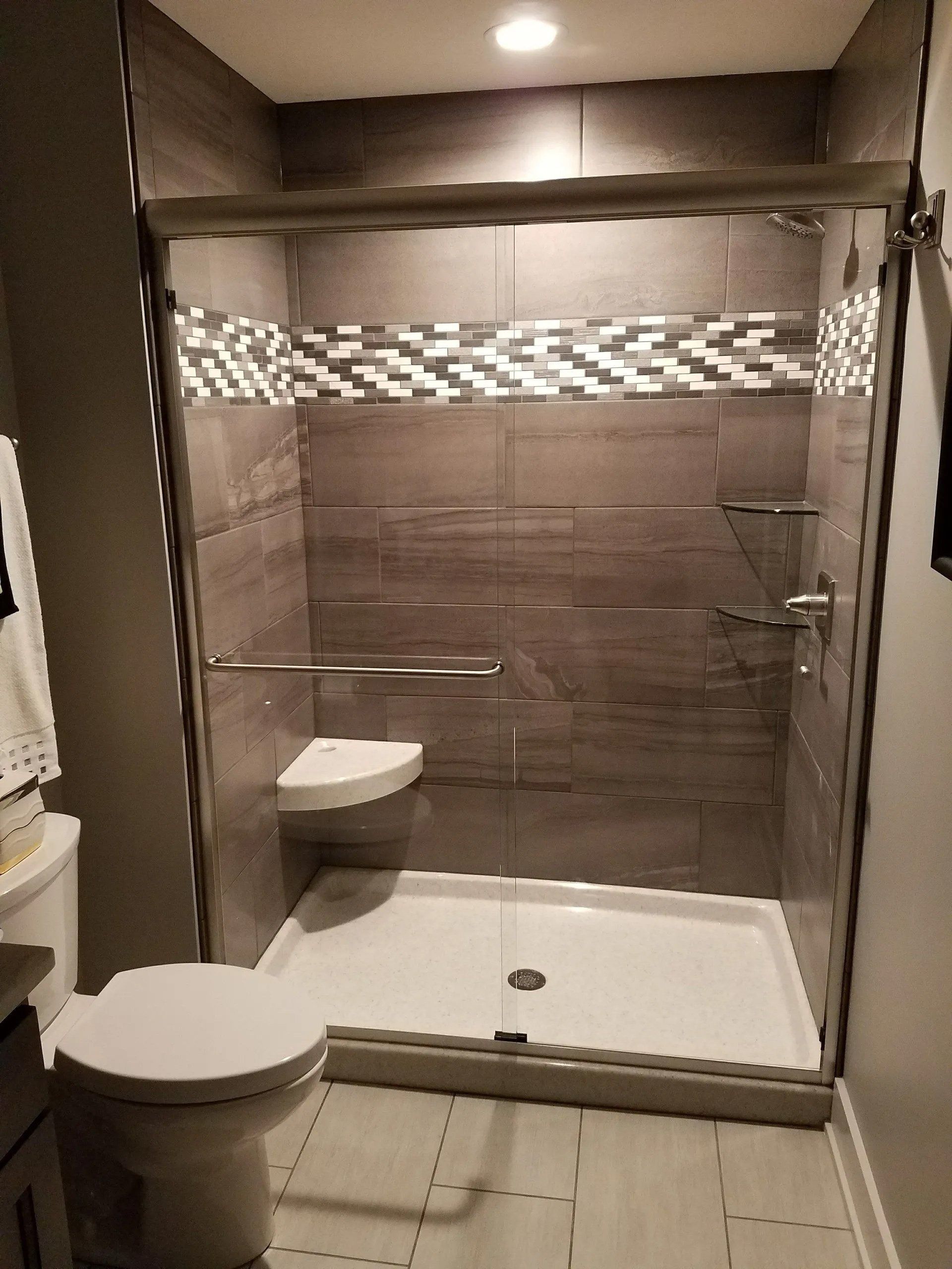 Small tiled bathroom with glass shower, wall-mounted toilet, and a toilet in the foreground.