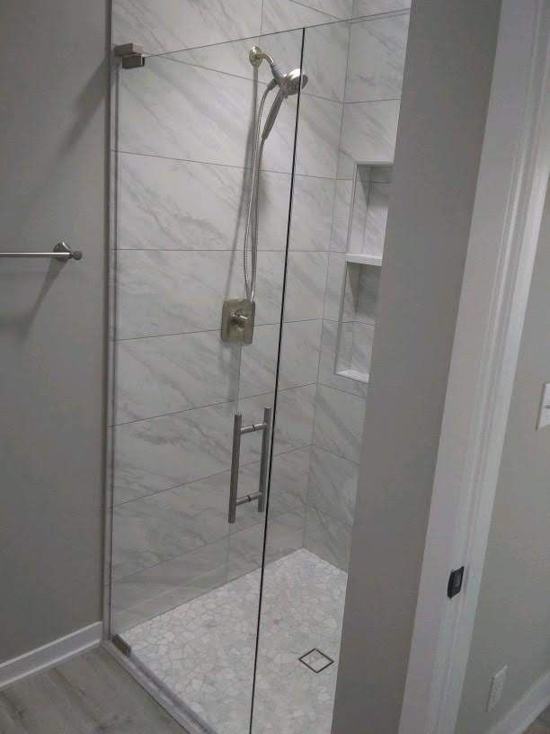 Glass walk-in shower with marble tile walls, chrome fixtures, and built-in shelves.