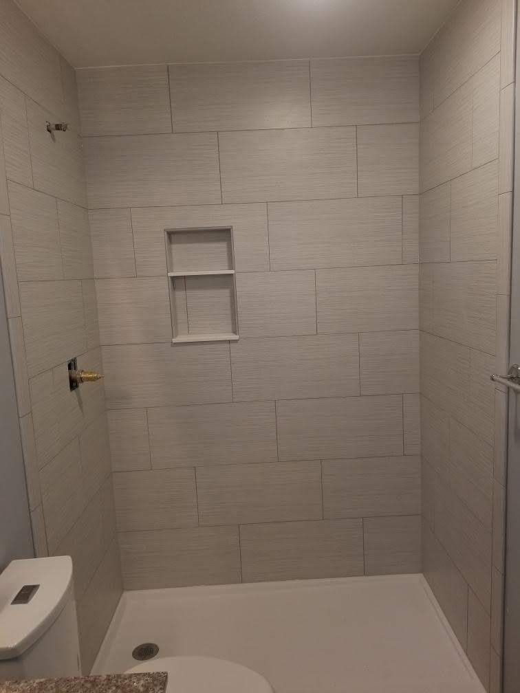 Empty tiled shower stall with built-in shelf and showerhead, viewed from the doorway.