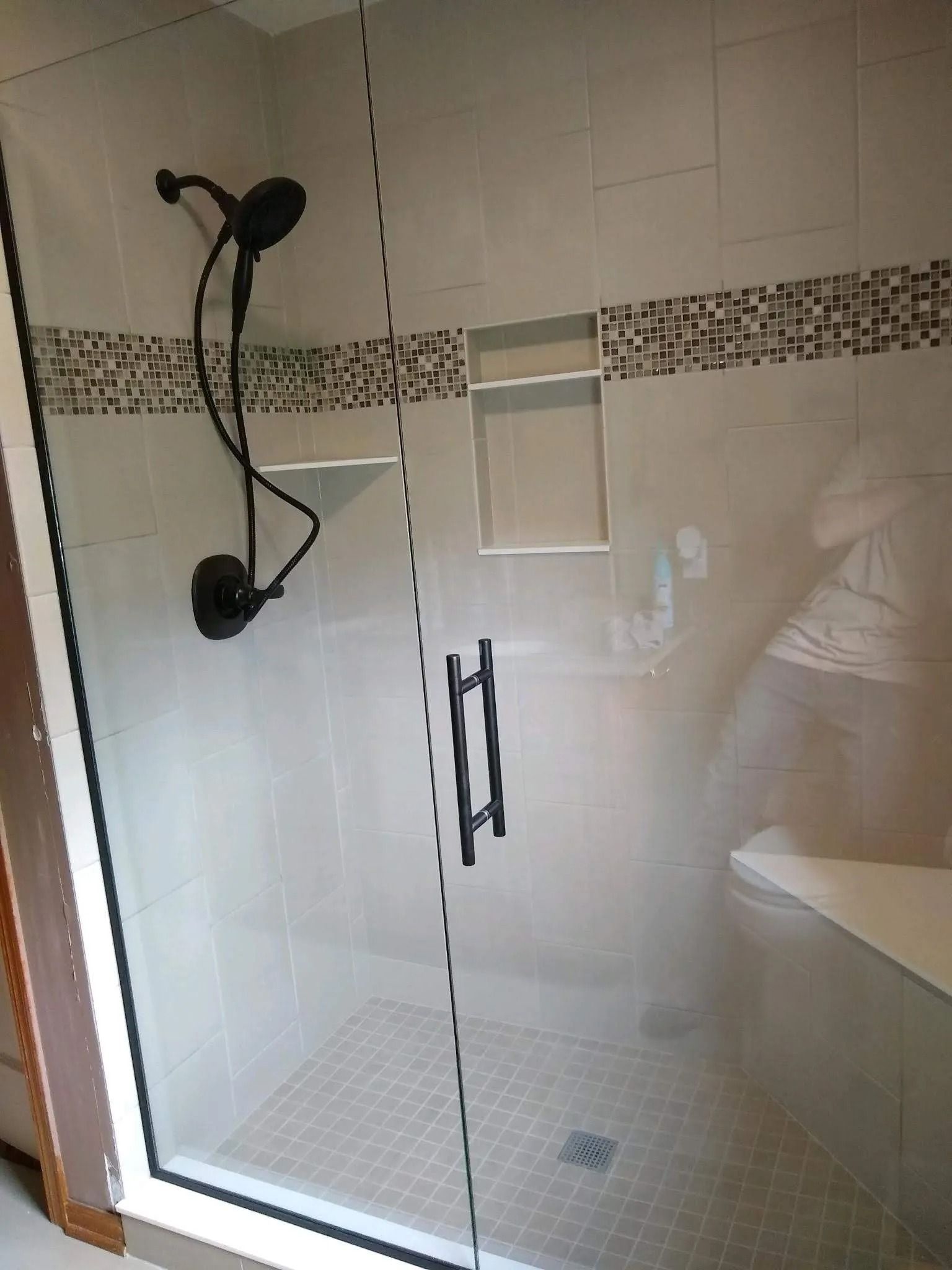 Glass shower stall with tiled walls, wall-mounted showerhead, and a tiled floor with a drain.