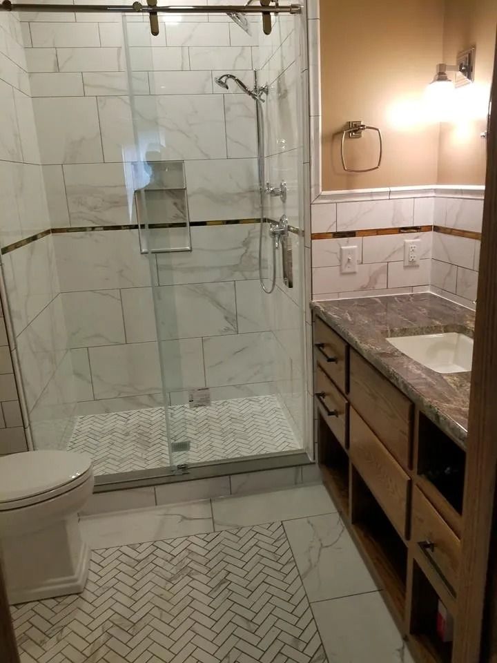 Bathroom with glass shower, vanity sink, toilet, and herringbone tile floor.