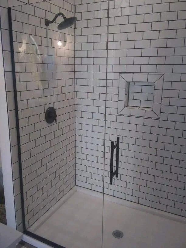 Walk-in shower with white subway tile, glass door, black fixtures, and a built-in shelf.