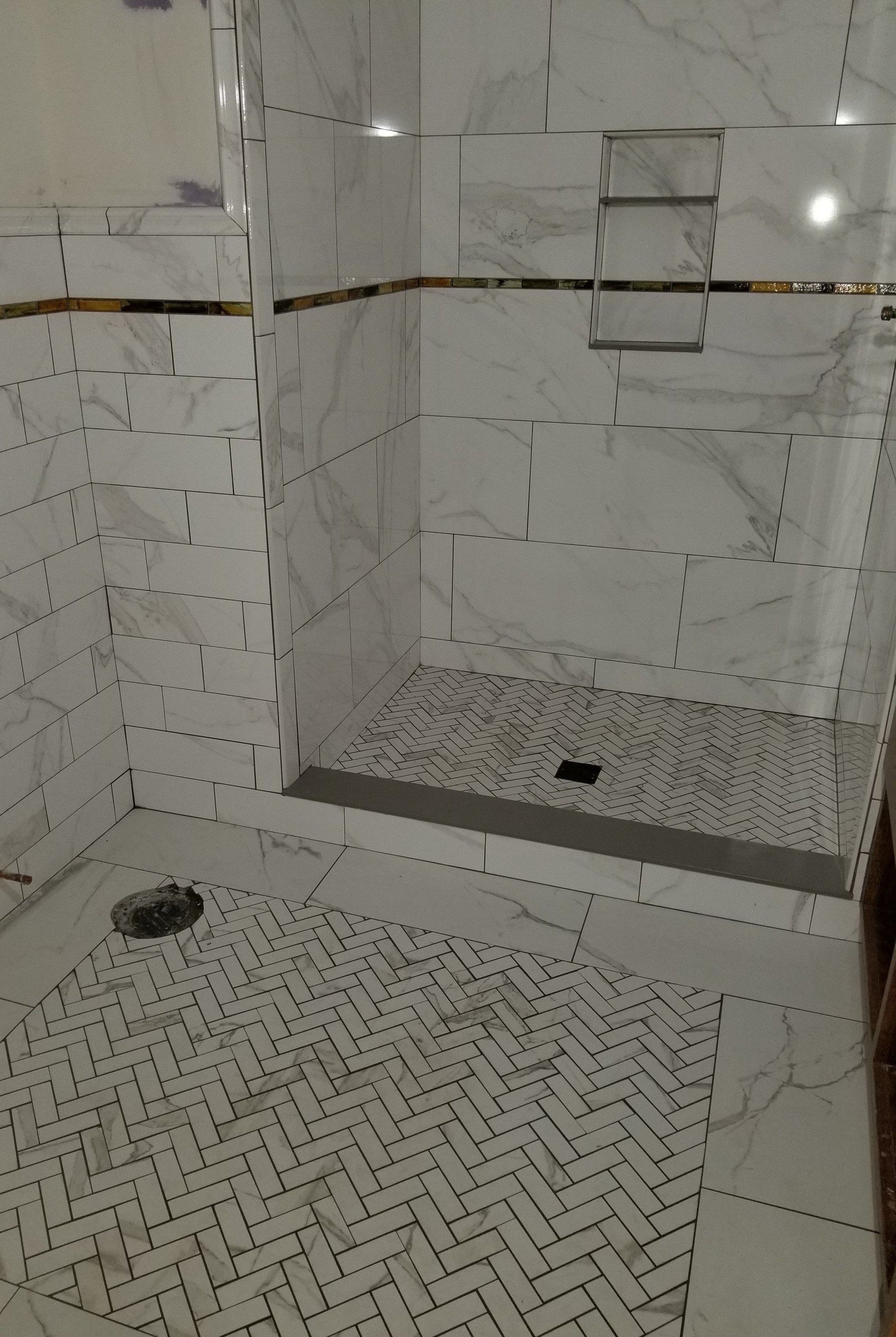 Tiled walk-in shower with hexagon floor tiles, white walls, and two drains