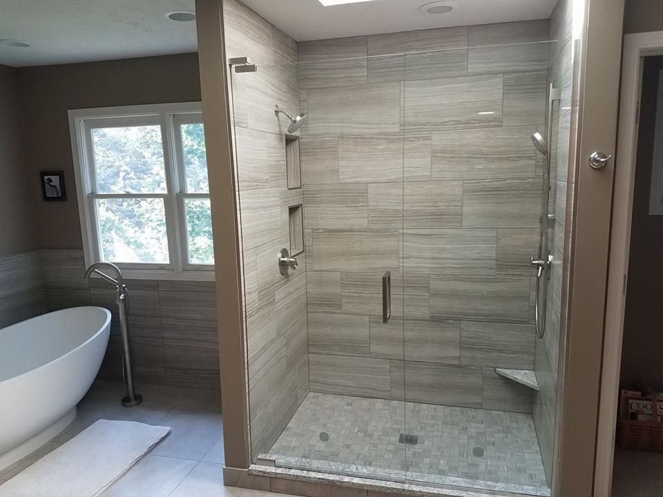Modern bathroom with a glass walk-in shower, tiled walls, and a freestanding tub by a window.