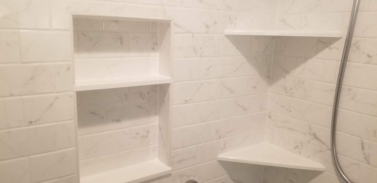White tiled shower with built-in shelves and corner ledges, plus a handheld shower hose on the right.