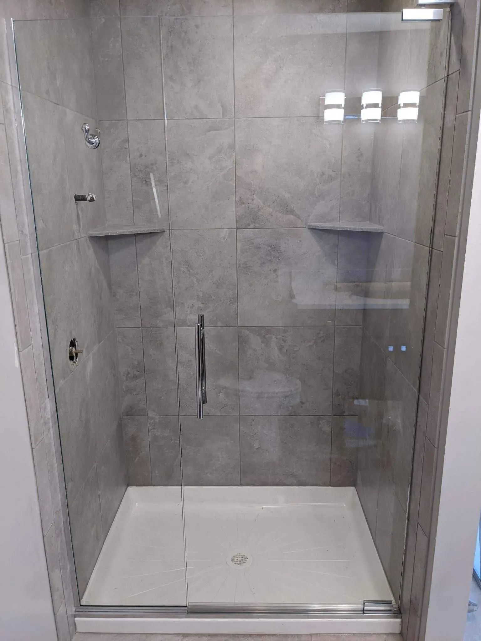 Modern tiled shower with glass door, white floor pan, and built-in corner shelves.