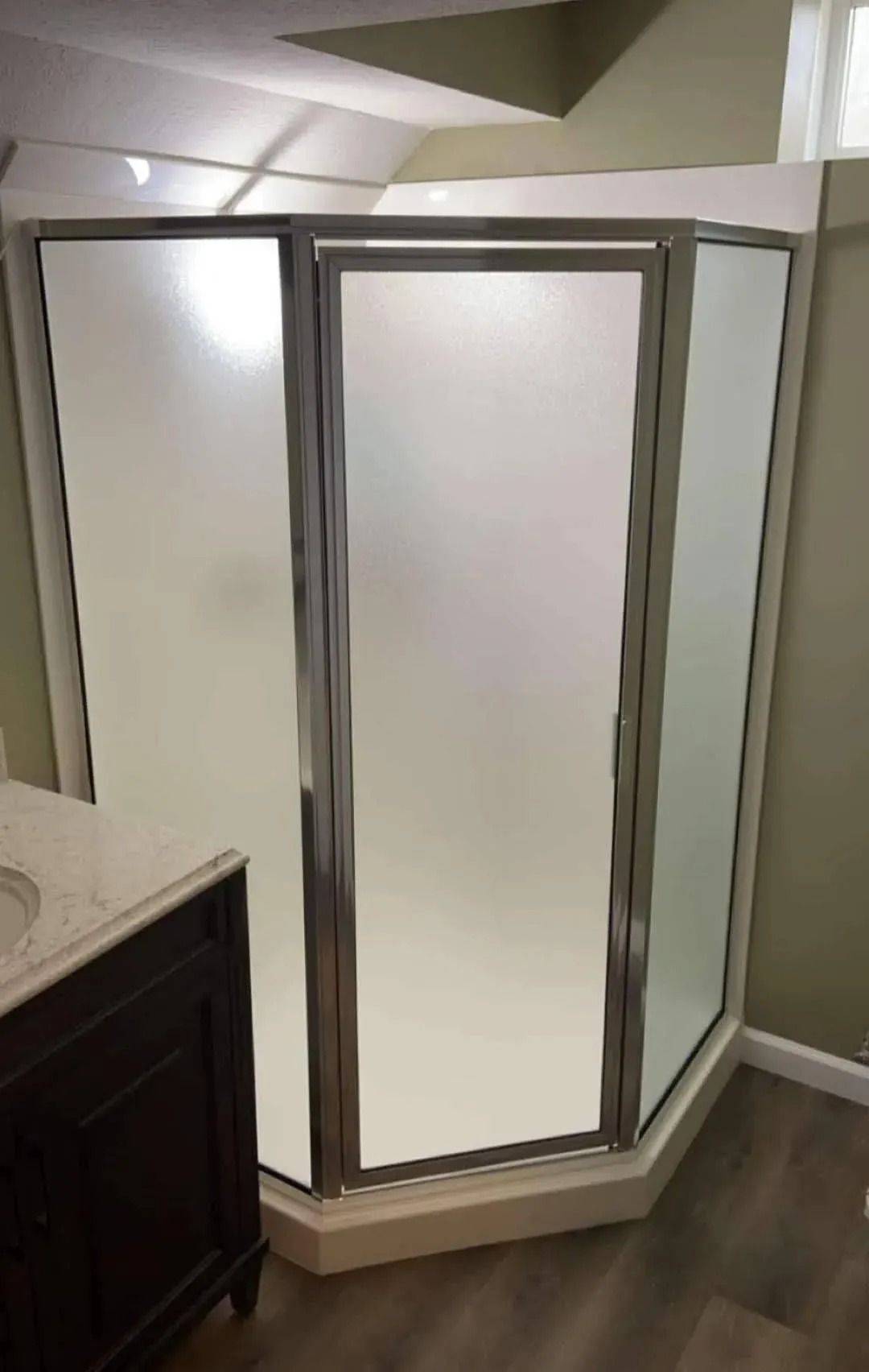 Corner shower enclosure with chrome-framed frosted glass panels in a bathroom.