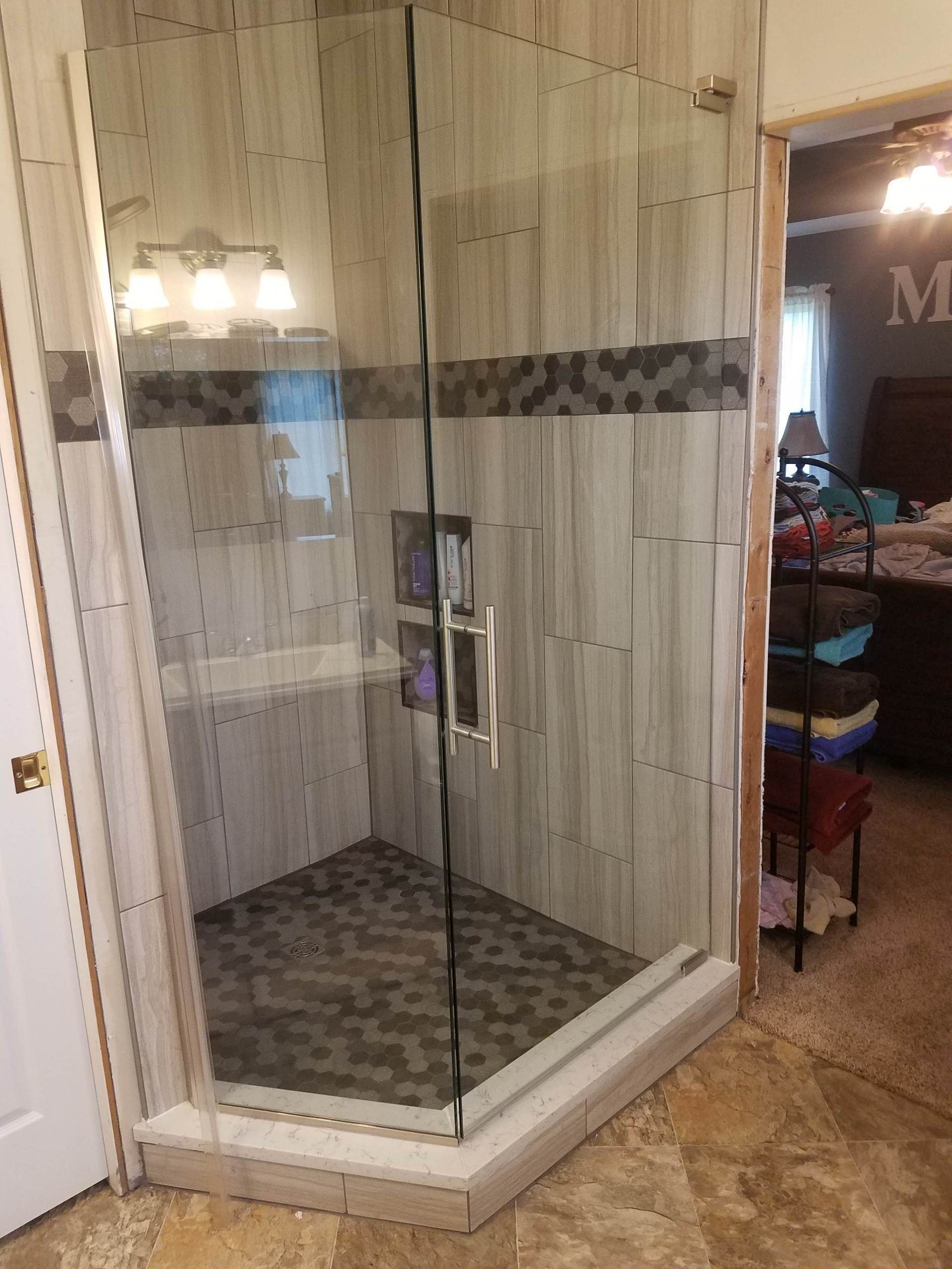 Glass shower enclosure with beige tile walls and a patterned floor in a bathroom