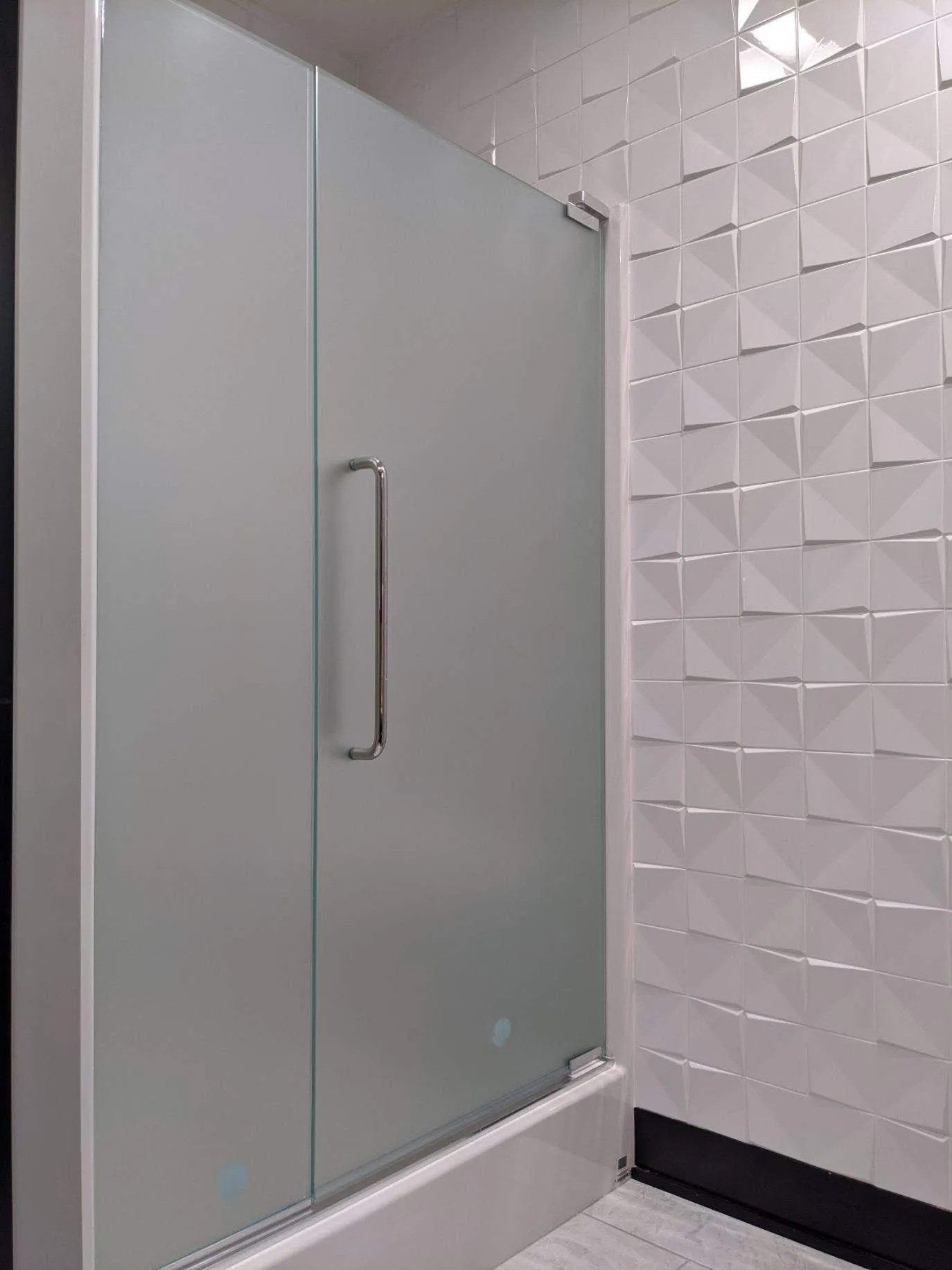 Frosted glass shower door beside a white textured bathroom wall.