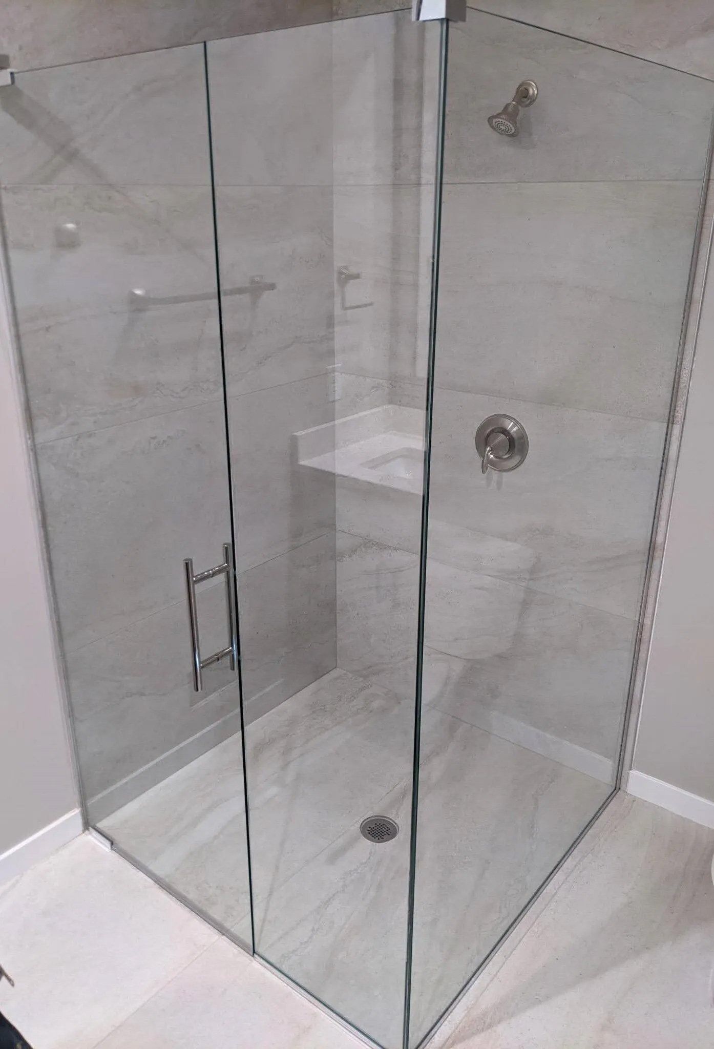 Corner glass shower enclosure with chrome handle and fixtures on a white bathroom floor