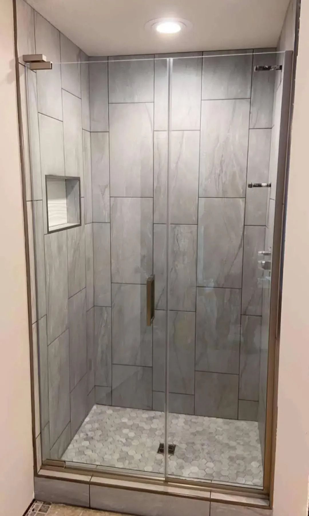 Modern tiled glass shower stall with a small built-in shelf and pebble stone floor