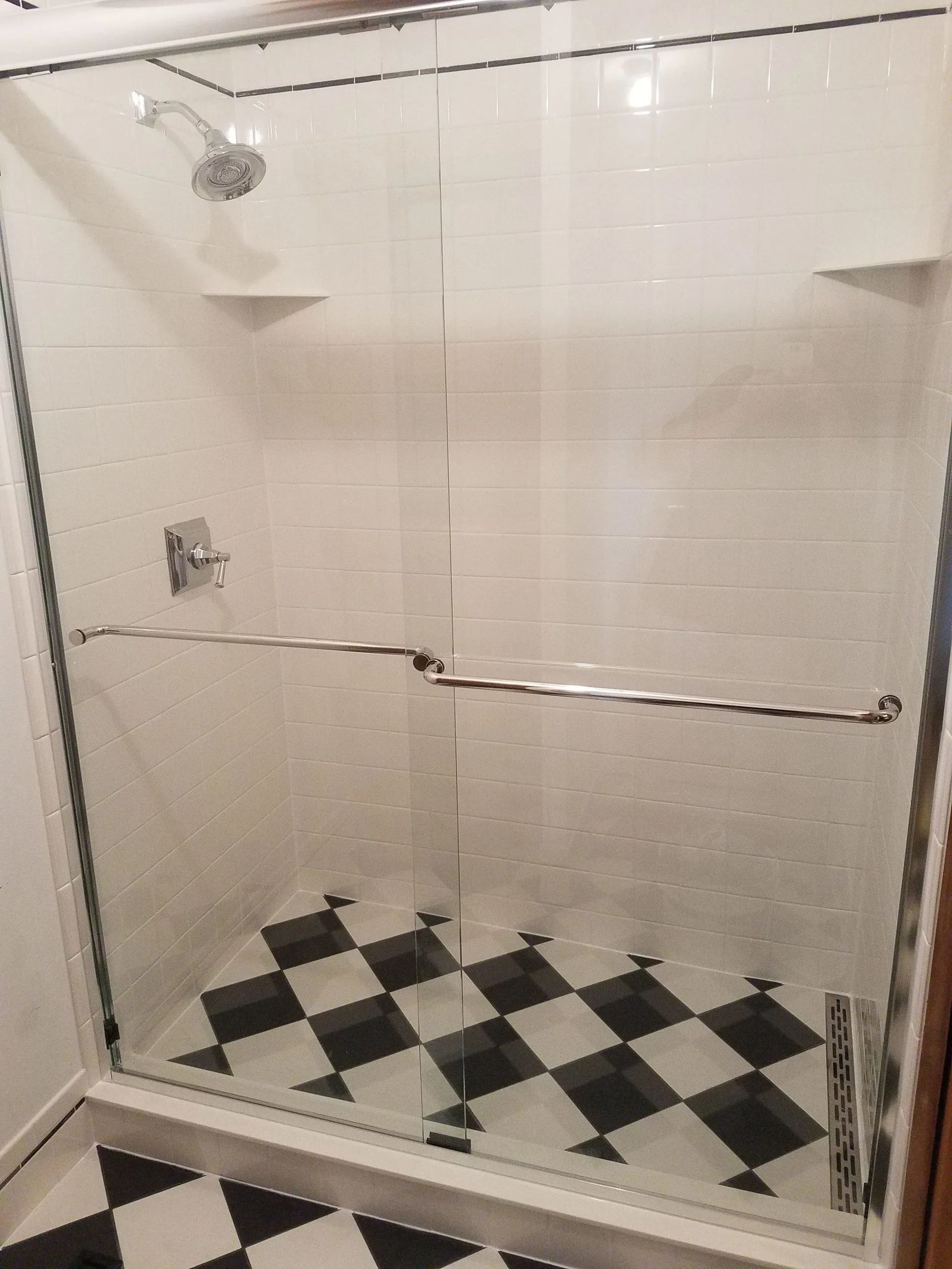 Glass shower enclosure with black-and-white checkered floor tiles and chrome hardware