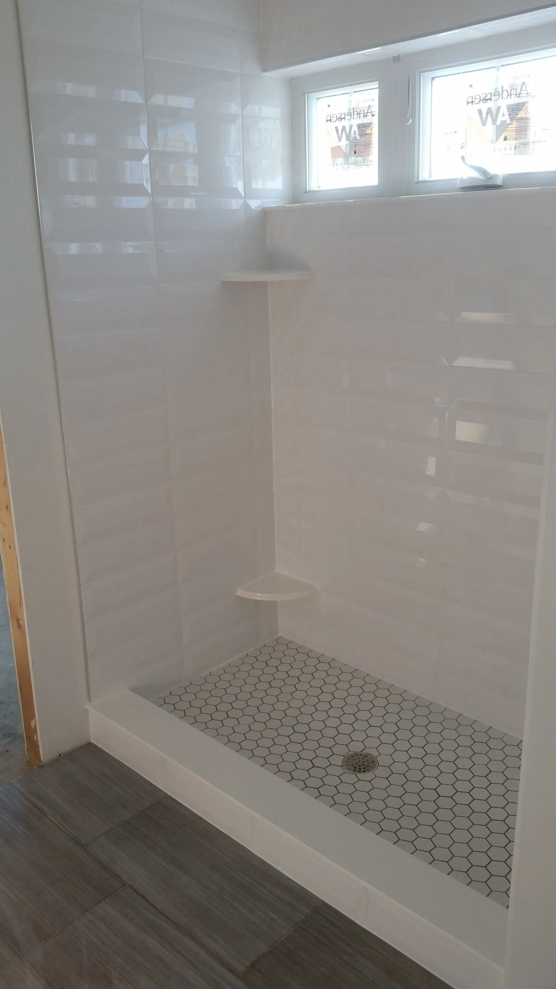 Modern tiled shower stall with a small corner shelf and mosaic floor drain in a bathroom