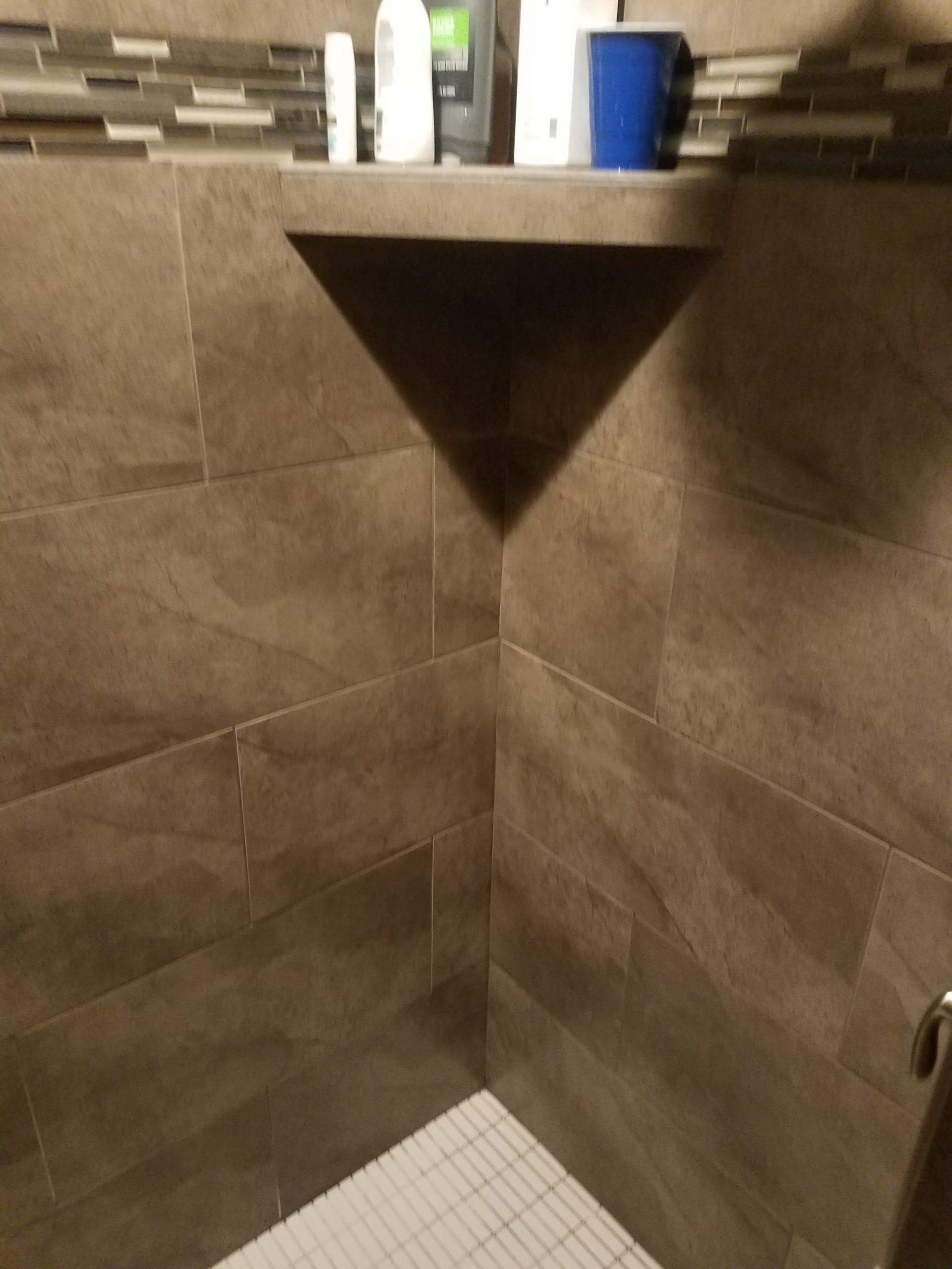 Tiled corner shower with a small corner shelf and a white shower floor drain