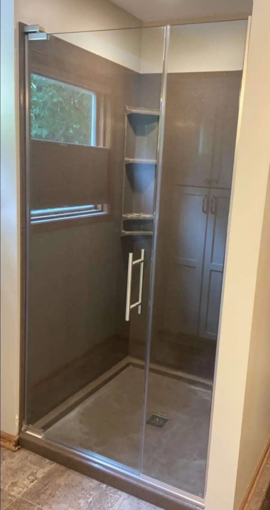 Glass walk-in shower with chrome fixtures and a built-in bench in a tiled bathroom.