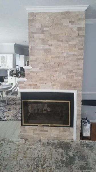 Brick fireplace with brass-trimmed glass doors in a living room, adjacent to a kitchen.
