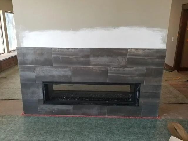 Partially tiled fireplace wall with a long black fireplace insert and white unfinished upper wall