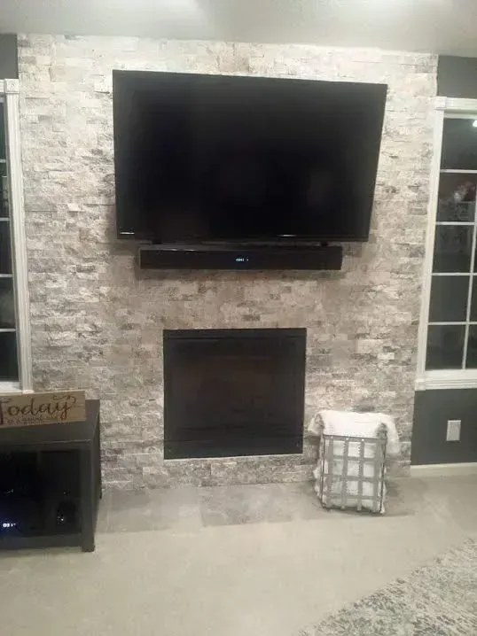 Living room wall with a mounted TV above a fireplace and stone accent surround