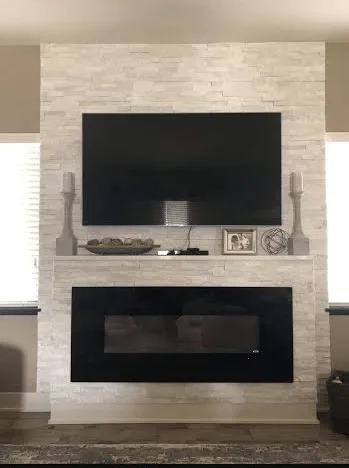 Stone fireplace wall with two flat-screen TVs and a mantel shelf with decor