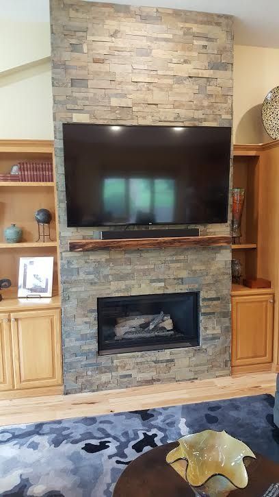 Living room with stacked-stone fireplace, mounted TV, built-in shelves, and a patterned rug
