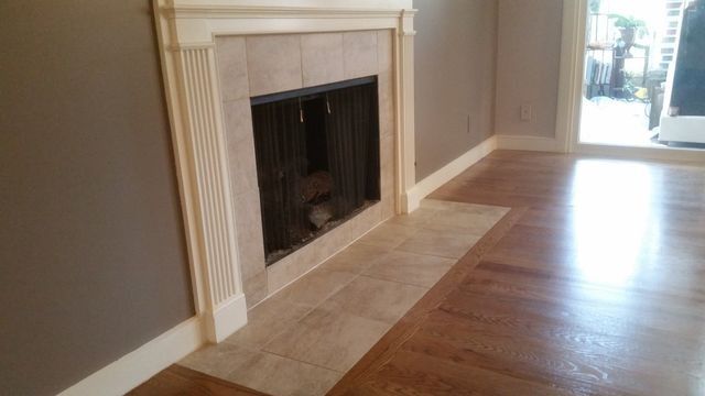 Empty living room with a white fireplace, beige tile hearth, and hardwood floors near a bright doorway