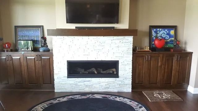 Living room with a white stone fireplace, wall-mounted TV, and wooden side cabinets with framed art.