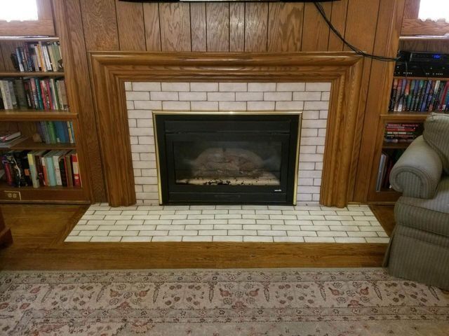 Wood-paneled living room fireplace with white tile surround, bookshelves, and a couch on the right