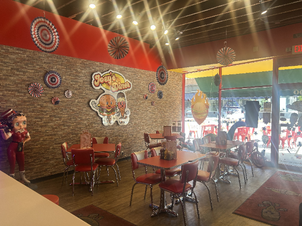 Interior of Joey's Pizza restaurant: red tables/chairs, stone-look wall, red/yellow accents, outdoor view.