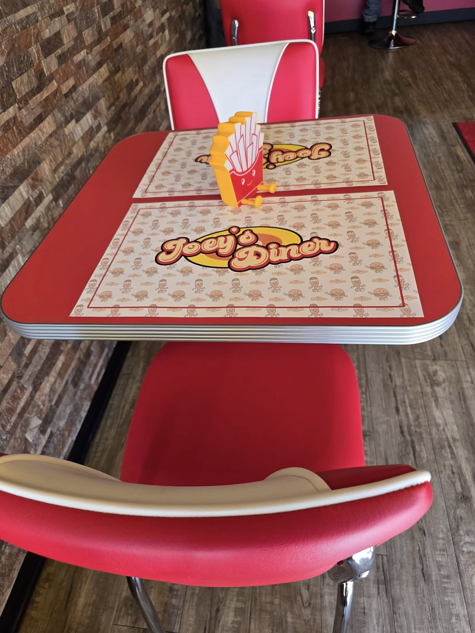 Red diner table with chairs, a french fry holder, and placemats.