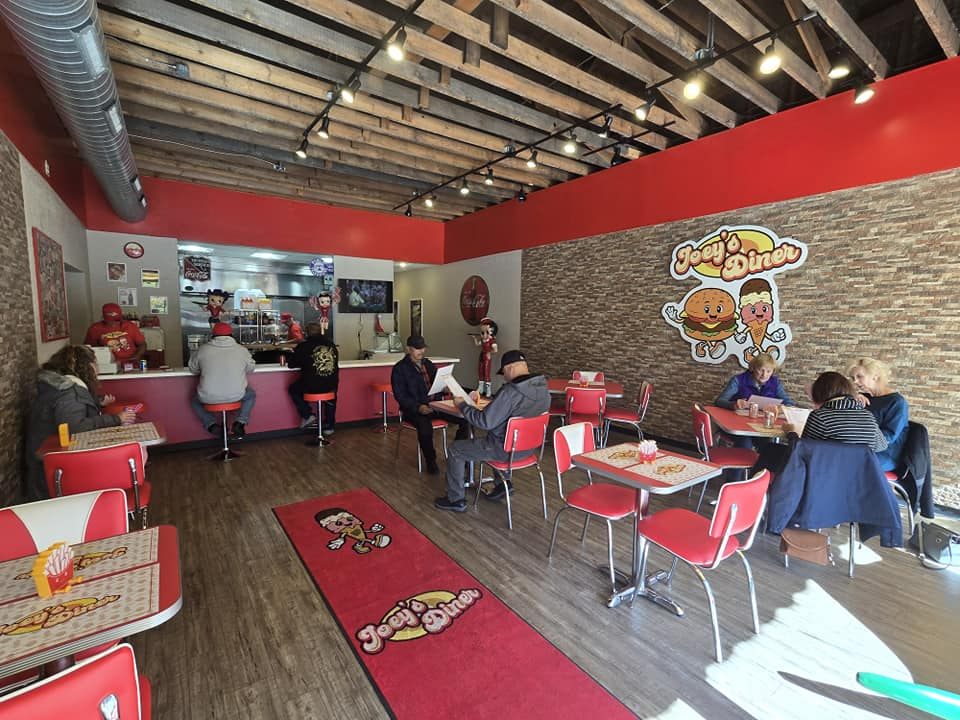 Interior of a diner with red and white booths, customers seated, and staff behind the counter.