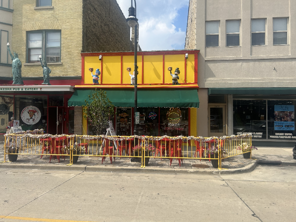 A yellow building with a green awning and outdoor seating; a street scene.