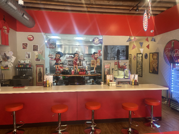 Red diner interior with counter seating, employees behind the bar, and red and white decor.