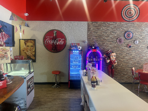 Retro diner interior with red accents, Coca-Cola sign, jukebox, and soda display.