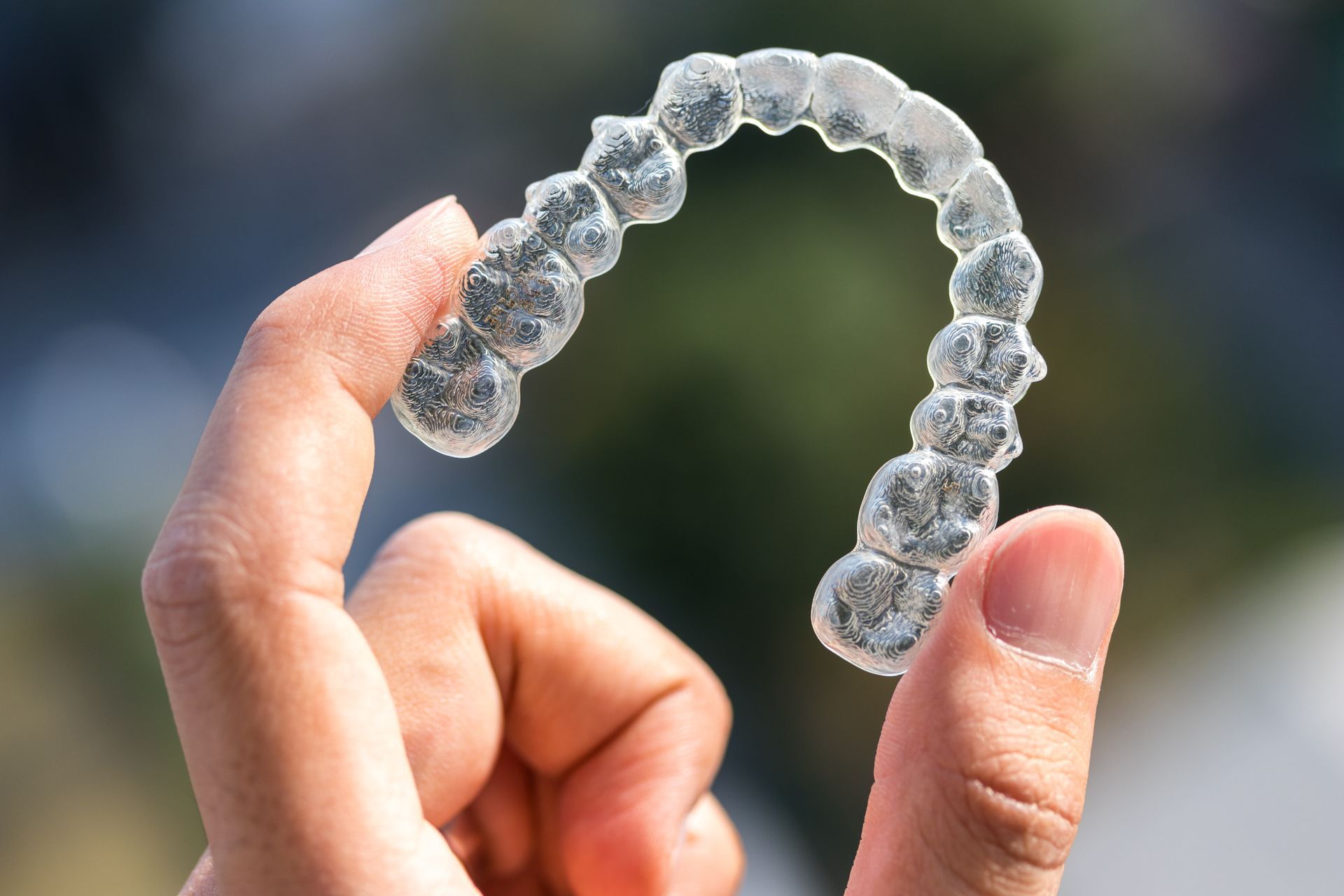 Hand holding a clear, horseshoe-shaped dental aligner.