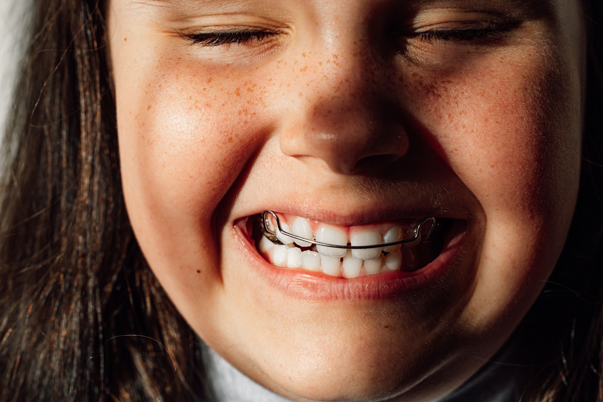 A young girl with braces on her teeth is smiling with her eyes closed.